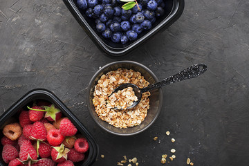 Black plastic containers take-away for a healthy snack food with raspberries, blueberries. Ingredients of healthy breakfast: granola, oat flakes, berries, nuts, apples, bananas. Top View.