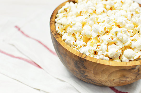 Brown wooden bowl with delicious traditional popcorn on a light wooden background. Top view of a light meal background.