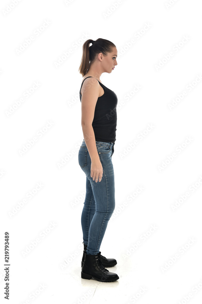 Poster  full length portrait of brunette girl wearing black single and jeans. standing pose in side profile. isolated on white studio background.