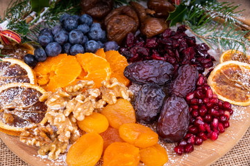 Platter of Festive Christmas Fruits.  Wooden Platter loaded with a selection of fresh and dried Christmas Fruits.  Decorated with Holly, Cinnamon and Christmas parcels.