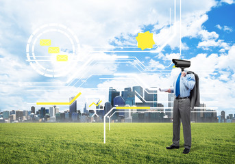 Camera headed man standing on green grass against modern cityscape
