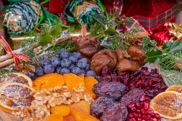Platter of Festive Christmas Fruits.  Wooden Platter loaded with a selection of fresh and dried Christmas Fruits.  Decorated with Holly, Cinnamon and Christmas parcels.