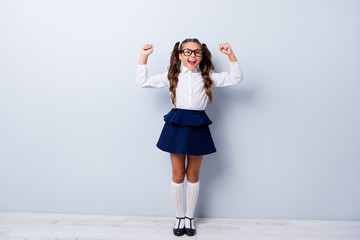 Full body size length of funny cute cheerful lovely stylish small little girl with curly pigtails in white formal blouse shirt, short blue skirt, raising hands up. Isolated over grey background