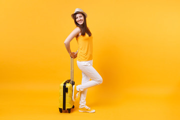 Traveler tourist woman in summer casual clothes, hat with suitcase isolated on yellow orange background. Female passenger traveling abroad to travel on weekends getaway. Air flight journey concept.