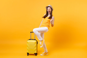 Tourist woman in summer casual clothes hat with suitcase clenching fists like winner isolated on yellow background. Passenger traveling abroad to travel on weekends getaway. Air flight journey concept