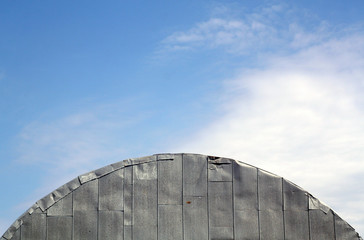 Roof of old metal hangar against cloudy sky.