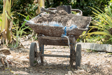 A soil with a hoe in old wheelbarrow in a tropical garden.