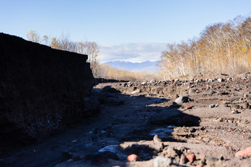 Road after mudflow. A lot of huge stones and dirt are everywhere. Blue sky and trees are around. Russia Autumn 2017 Kamchatka.