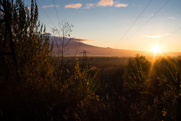 Sunrise is during great morning in mountains. Beautiful grass and trees are under warm light. Sky is highlighted by the sun. Golden autumn in mountains.