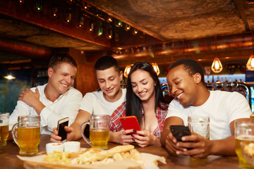 Happy friends using smartphone and having fun with beer and snacks.