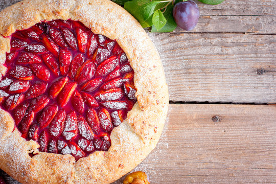 Galette on a curd pastry with plums on a wooden table, top view, copy space