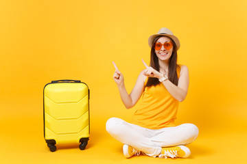 Traveler tourist woman in summer casual clothes, hat sit with suitcase isolated on yellow orange...