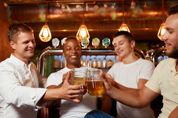 Four friends raising glasses of beer and celebrating their friendship in cozy pub.