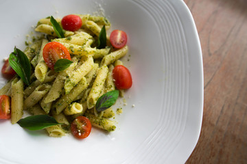 Pasta with tomato sauce and basil in white dish on wooden background. Italian food for vegetarian and healthy.