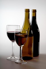 A glass of white wine and a glass of red wine next to bottles of