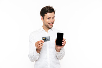 Caucasian man with dark hair smiling while holding smartphone and credit card, isolated over white background