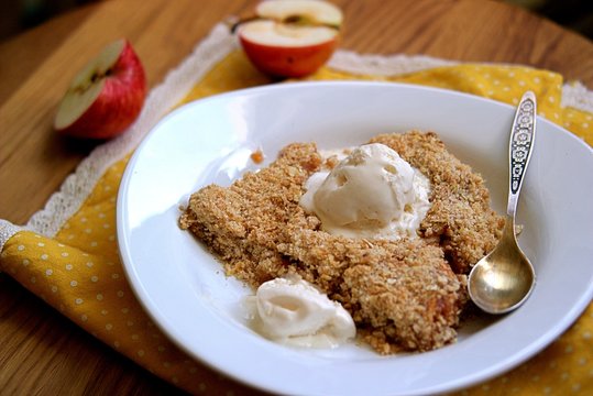 Apple crumble pie with whole-grain flour, oat flakes and cinnamon. Served warm with a vanilla ice cream ball..