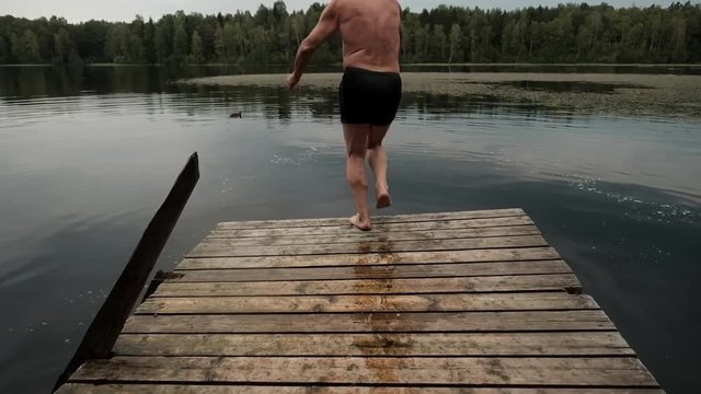 Caucasian mature man jumping from wooden pier in lake. Having fun in vacation in country side.