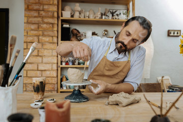 Little pots. Dark-haired potter wearing dark brown apron forming little pots using pottery wheel