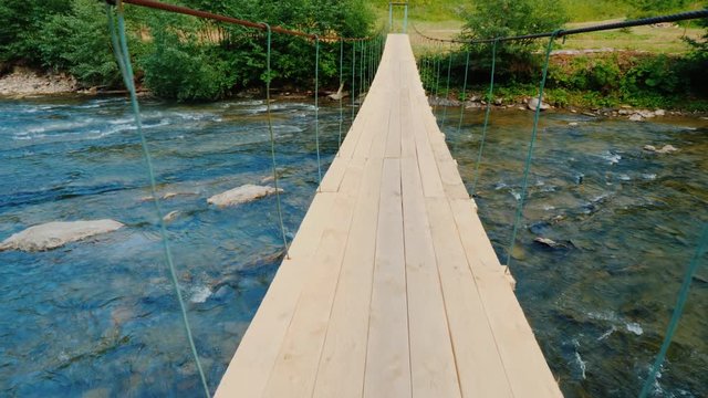 Walk on a shaky bridge across a rough mountain river. Pov video