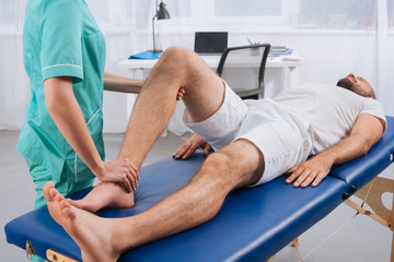 Obraz premium partial view of female massage therapist doing massage to patient on massage table in clinic