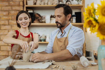 Clay item. Beaming dark-haired woman wearing red shirt and brown apron making clay item