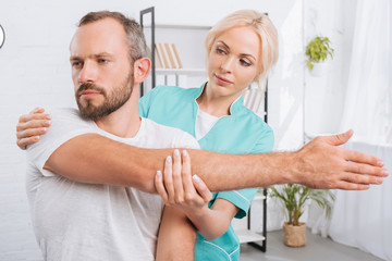 portrait of physiotherapist stretching mans arm in hospital