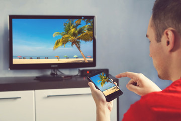 Mature Man With Smartphone Connected To A TV Watching Movie At Home