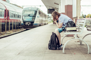 Sad young woman sitting on a banch in a train station.  Teen waiting for the train in the middle of...