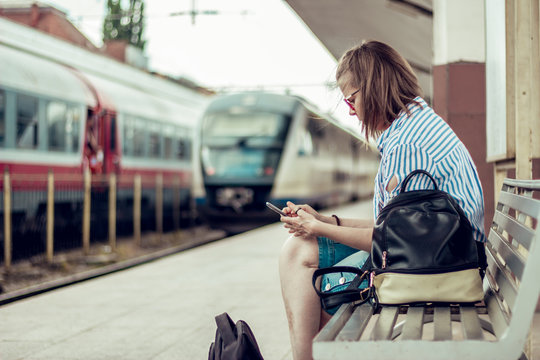 Girl using a mobile phone in a train station. Young woman sitting texing on a smartphone