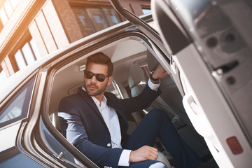 Confident businessman. Fashionable man coming out of a car