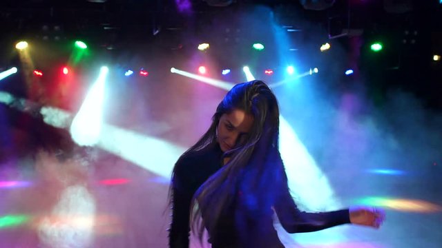 A sexy girl with luxurious long hair dances in a nightclub. A gorgeous girl flirts and dances at a party in the dark under the spotlight, slow motion.