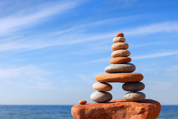 Fototapeta na wymiar Rock zen pyramid of white and pink pebbles on a background of blue sky and sea.