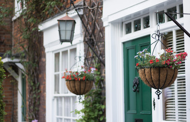 Beautiful traditional house front: flower baskets, a lantern, an entrance door, a window, a brick wall. Concept: English lifestyle and gardening.