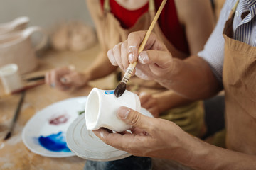 Painting brush. Male potter holding painting brush while decorating clay pot finishing his work day