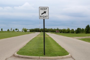 A keep right sign at the crossroad on a cloudy day.