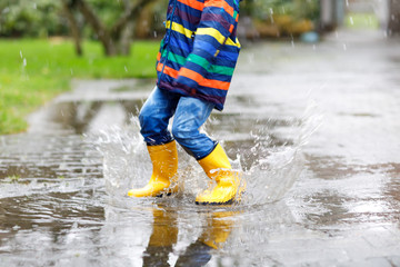 Close-up of kid wearing yellow rain boots and walking during sleet, rain and snow on cold day....