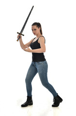 Fototapeta na wymiar full length portrait of brunette girl wearing black single and jeans. standing pose holding a sword. isolated on white studio background.