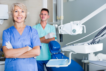 Portrait of friendly woman dentist arms crossed with dental assistant behind