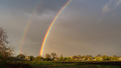 A double rainbow against the background of a dark sky. Rural landscape.