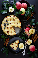 American tradition apple pie with apples, blueberry and cinnamon decorated apple leaves on dark wooden background. Top view. Flat lay. Still life.