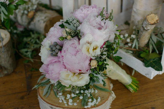 Pale pink colored peonies, freesias and greenery bouquet sitting on top of a rustic wooden table, floral arrangement for the bride, perfect accessory for wedding ceremony