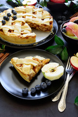 American tradition apple pie with apples, blueberry and cinnamon decorated apple leaves on dark wooden background. Flat lay. Still life.