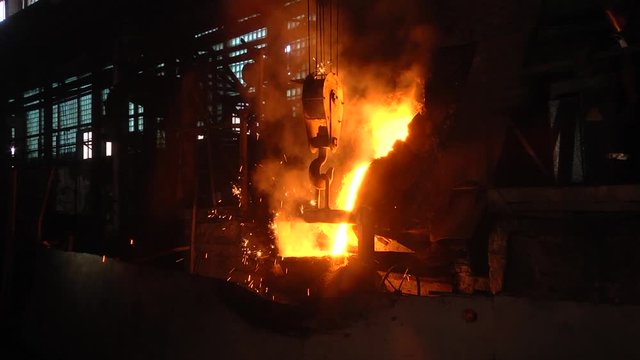 Room for the manufacture of metal products by casting. Casting shop for gasified models. The molten metal is poured from the induction furnace into the ladle. Sparks of hot metal fly apart.