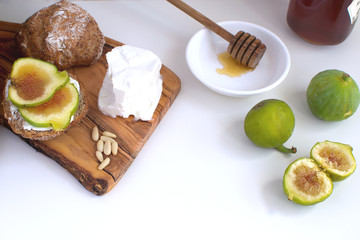 Fresh green figs Wooden cutboard Wholegrain bread Honey Goat cheese Pine nuts Healthy eating concept Canapes Sandwiches Appetizer Copy space White background