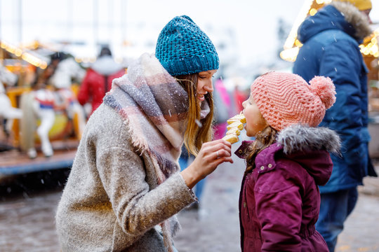 Young mother and daughter eating white chocolate covered fruits on skewer on traditional German Christmas market. Happy girl and woman on traditional family market in Germany, Munich during snowy day.