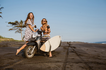 laughing couple with scooter and surfboard on beach in bali, indonesia