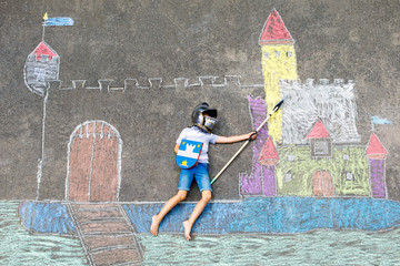 Little active kid boy drawing knight castle and fortress with colorful chalks on asphalt. Happy...