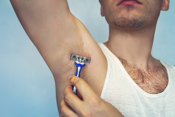 underarm hair removal. Male depilation. Young attractive muscular man using razor to remove hair...
