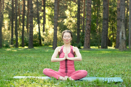 Beautiful young female make a yoga training in a sunny summer forest. Women's health concept photo.